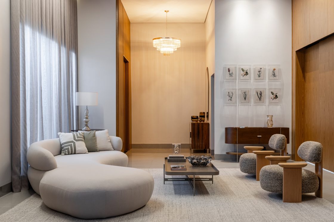 Living amplo com sofá orgânico cinza, tapete, mesa de centro e lustre ao fundo, tudo em tons neutros quentes