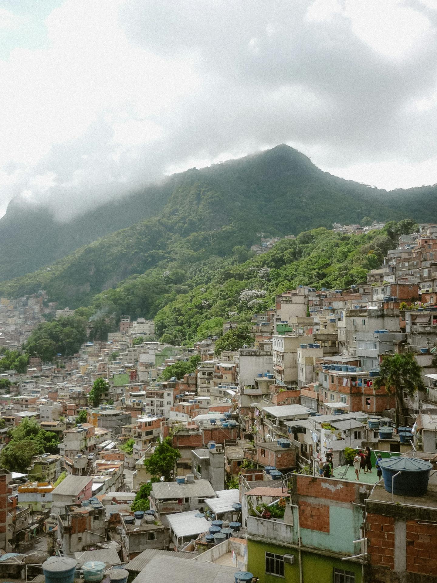 Vista ampla de comunidade construída em morro do Rio de Janeiro, com moradias erguidas em declive acentuado e cercadas por vegetação densa
