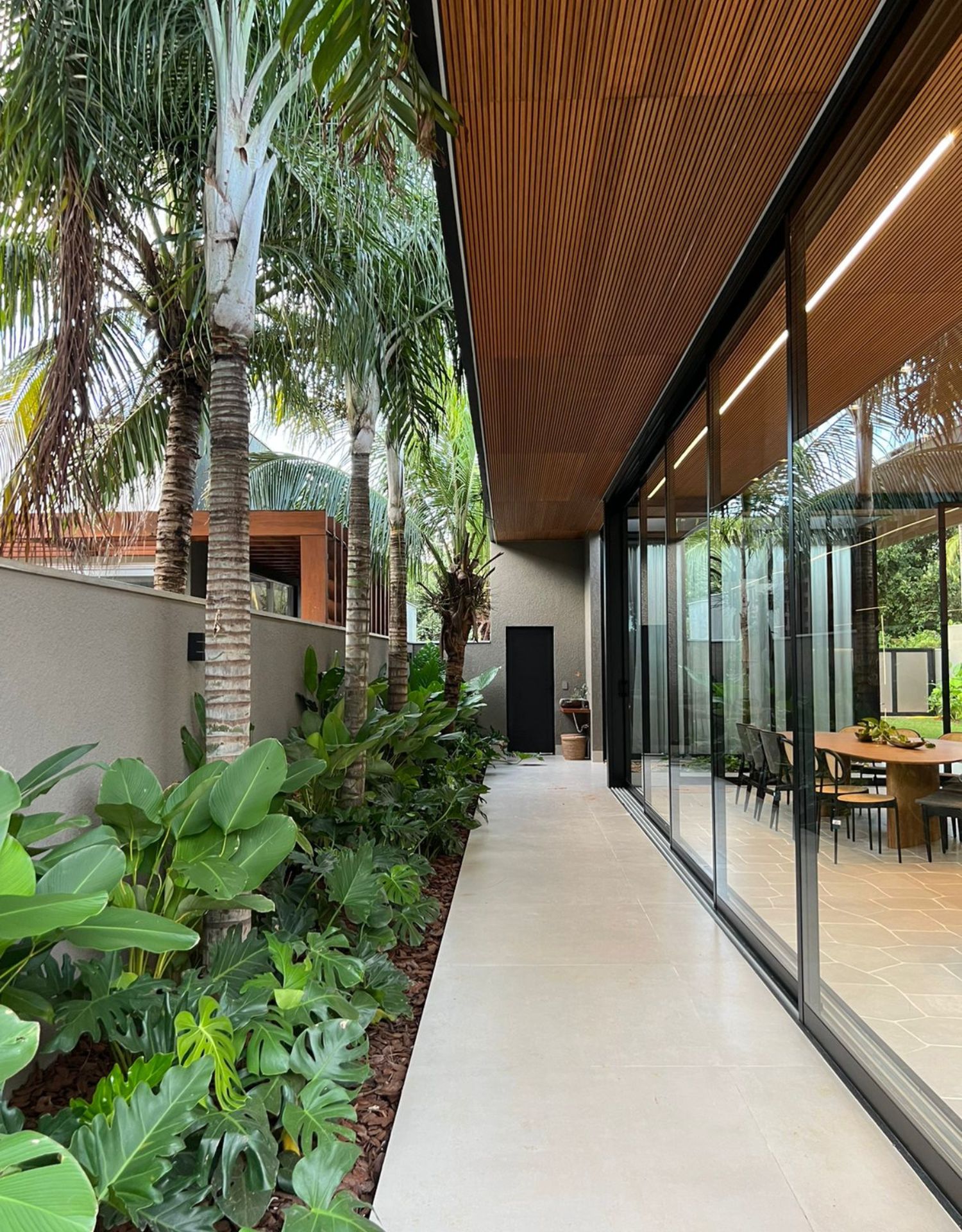 Corredor externo com piso claro em porcelanato, projeto paisagístico e teto em madeira