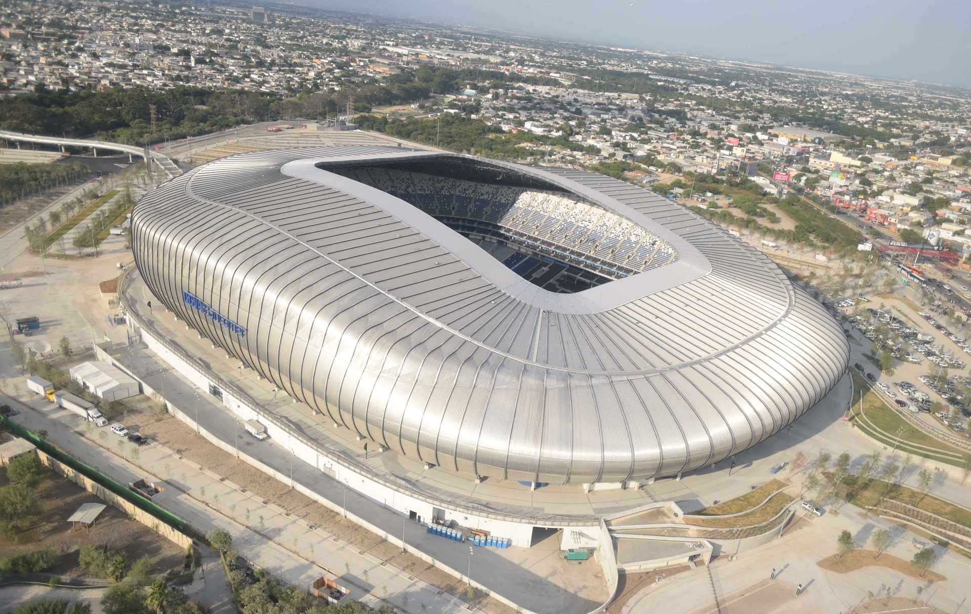 Vista aérea do Estádio Monterrey (Estadio BBVA), com fachada metálica prateada de grandes proporções e tecido urbano ao redor