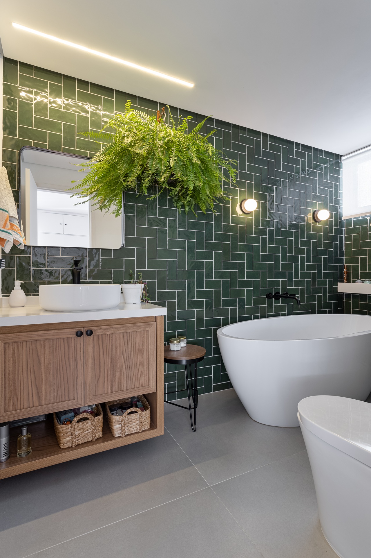 Banheiro com parede em azulejo verde, móvel de madeira e banheira vitoriana