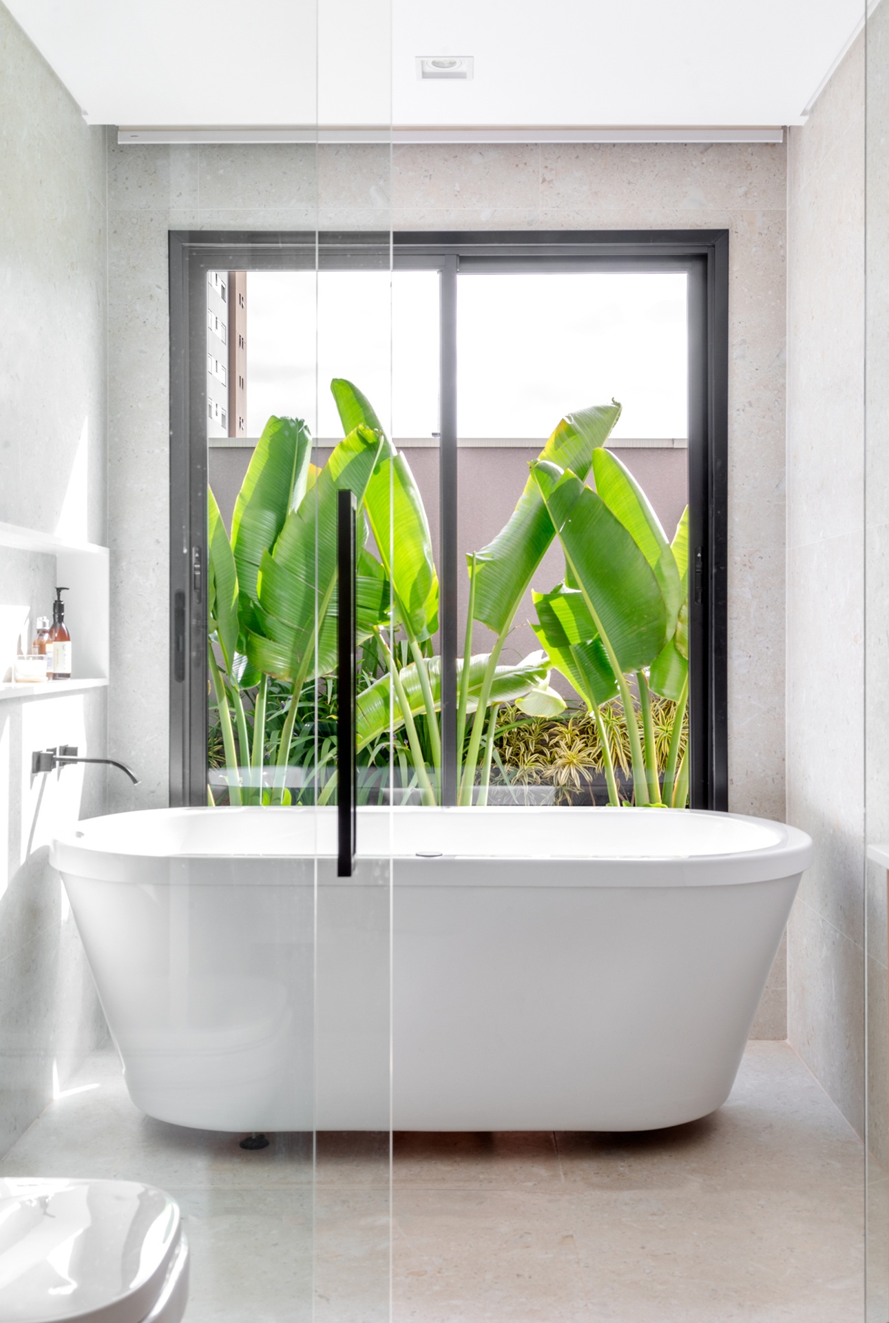 Banheiro branco com banheira no box e vista para exterior com plantas