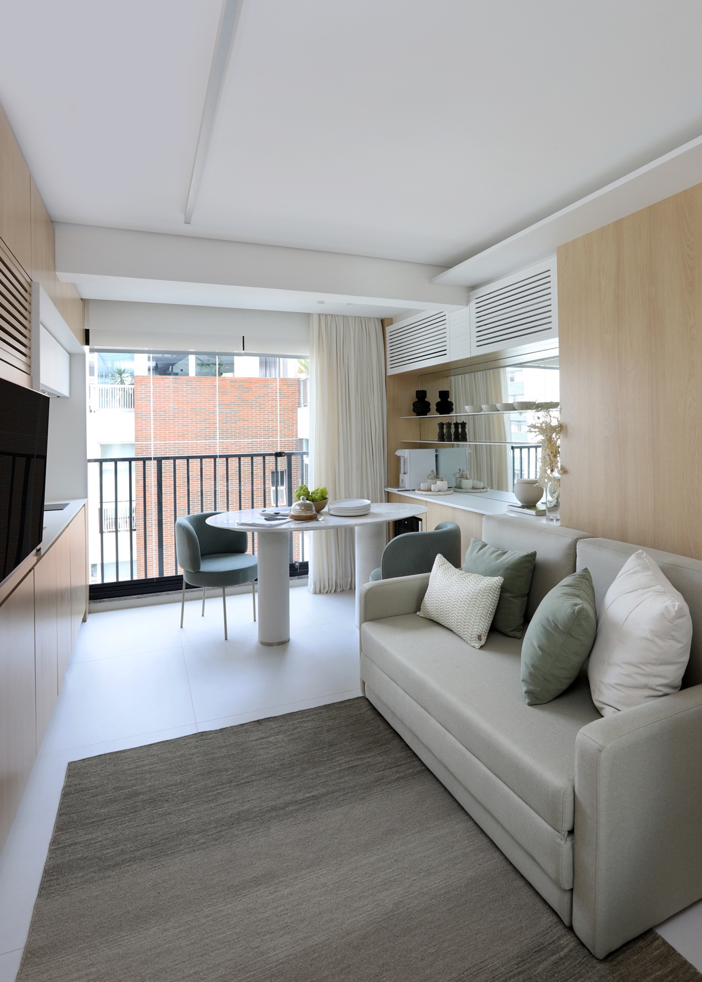 Sala de apartamento integrada à varanda com decoração em tons claros e neutros e porta de correr atrás de sofá