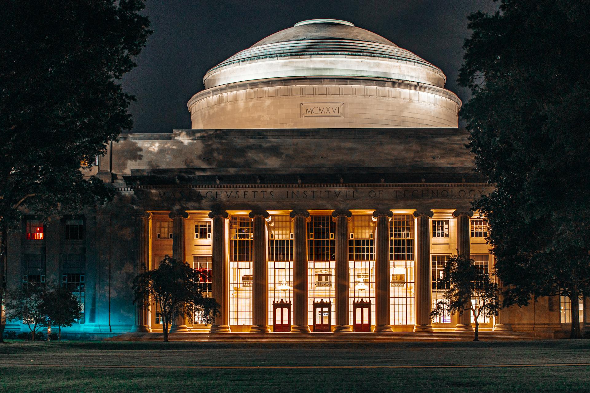 Edifício do Massachusetts Institute of Technology iluminado à noite, com fachada neoclássica, colunas monumentais e cúpula central
