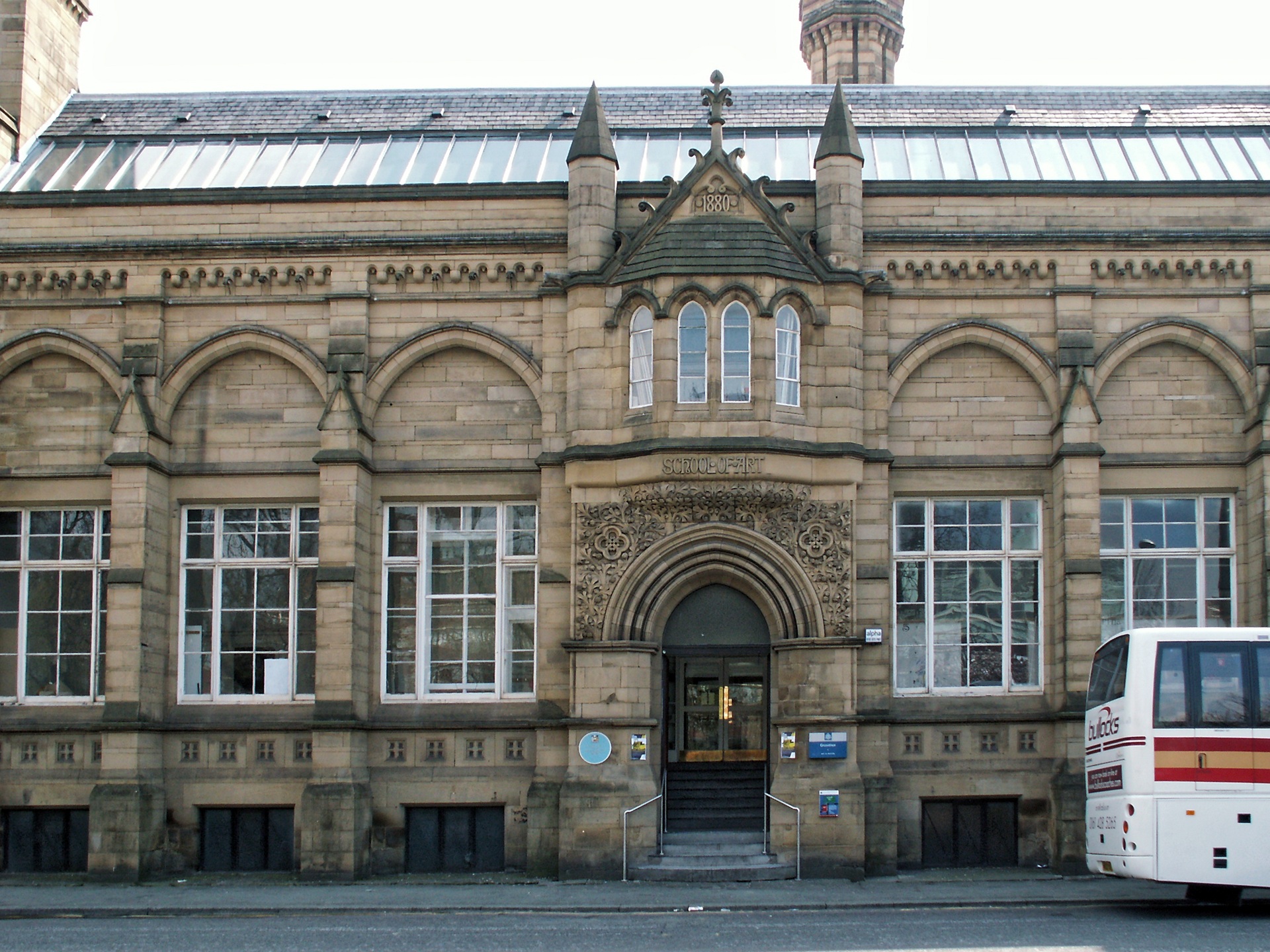 Fachada histórica da Manchester School of Architecture, no Reino Unido, com elementos em pedra, arcos e janelas simétricas