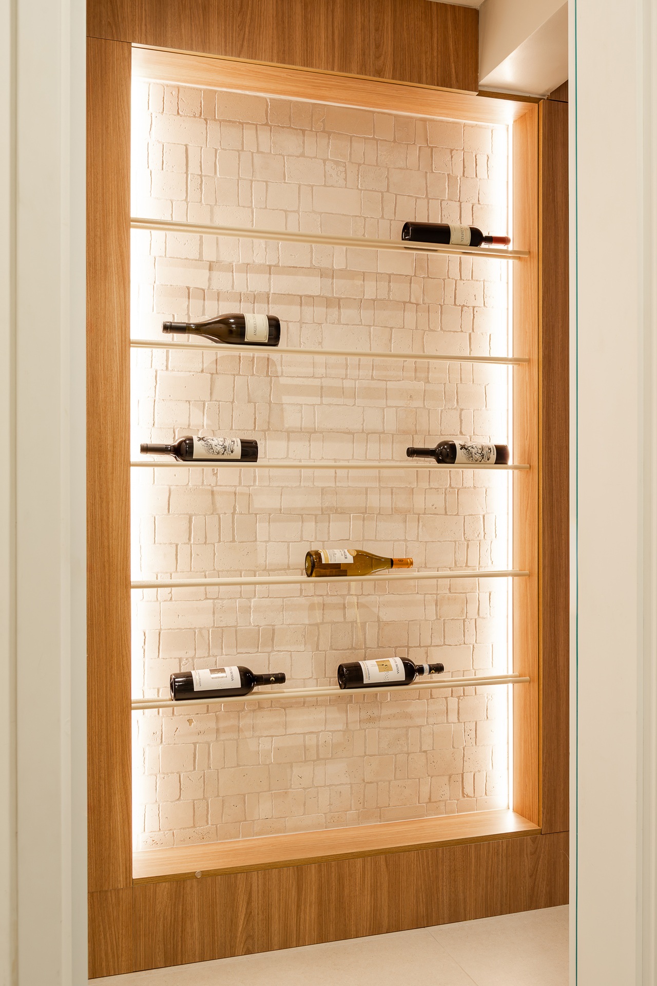 Nicho de parede para vinhos com iluminação direcionada e fundo em mosaico branco com relevo