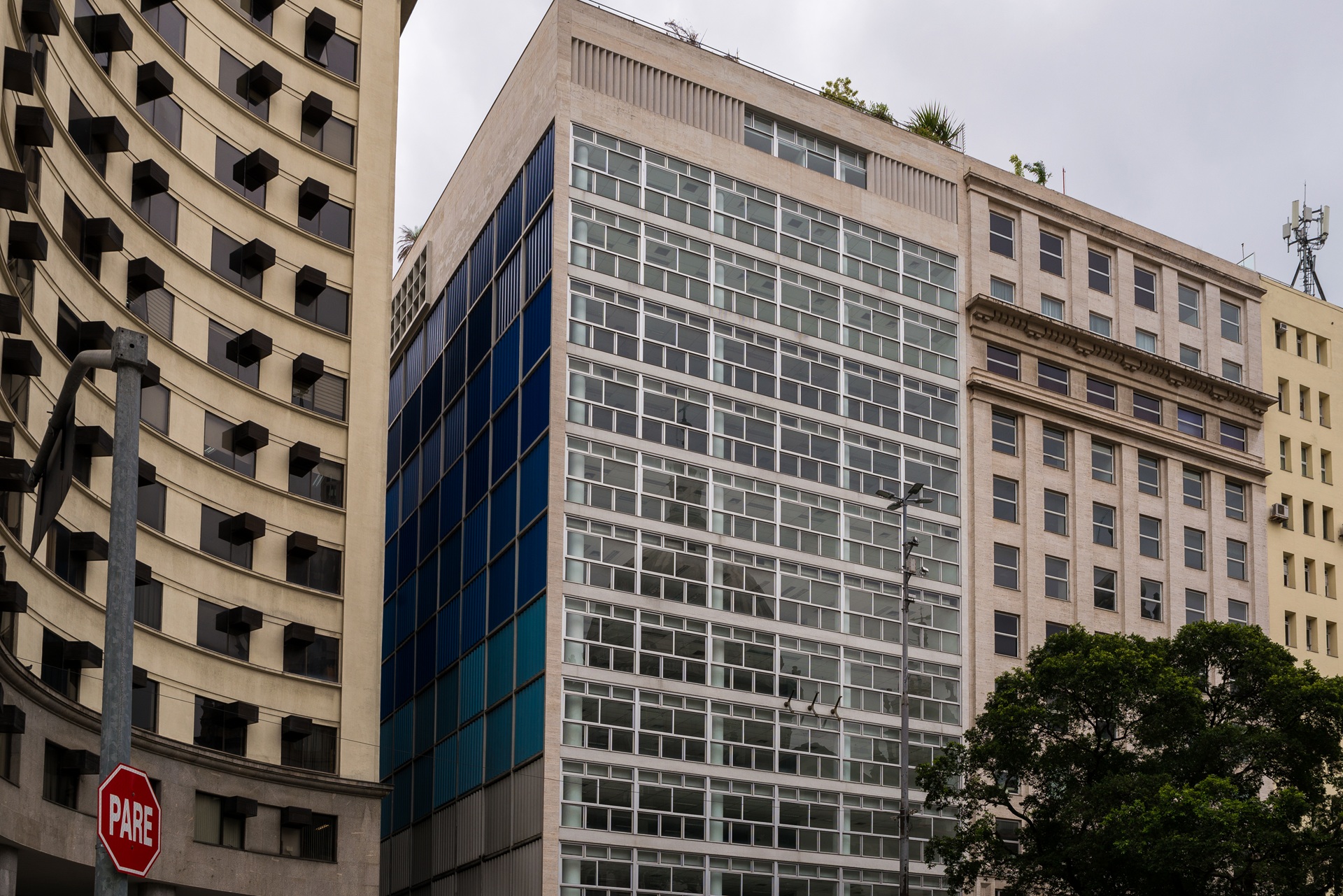 Vista externa da sede do antigo Banco Boavista, projeto de Oscar Niemeyer no centro do Rio de Janeiro, com volume retangular elevado, fachada envidraçada com brises e integração ao tecido urbano ao redor