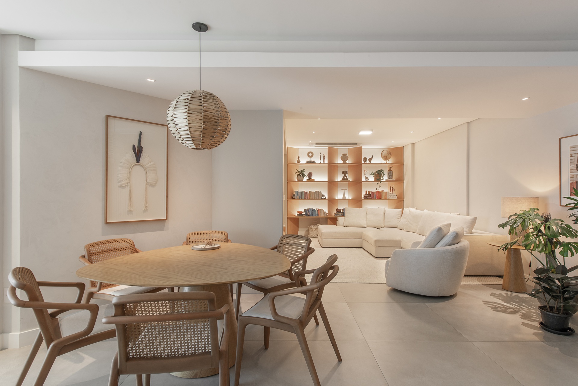 Ambiente integrado de sala de estar e jantar com linguagem contemporânea, paleta clara e iluminação abundante. A mesa de jantar em madeira recebe um pendente de palha trançada como ponto de destaque