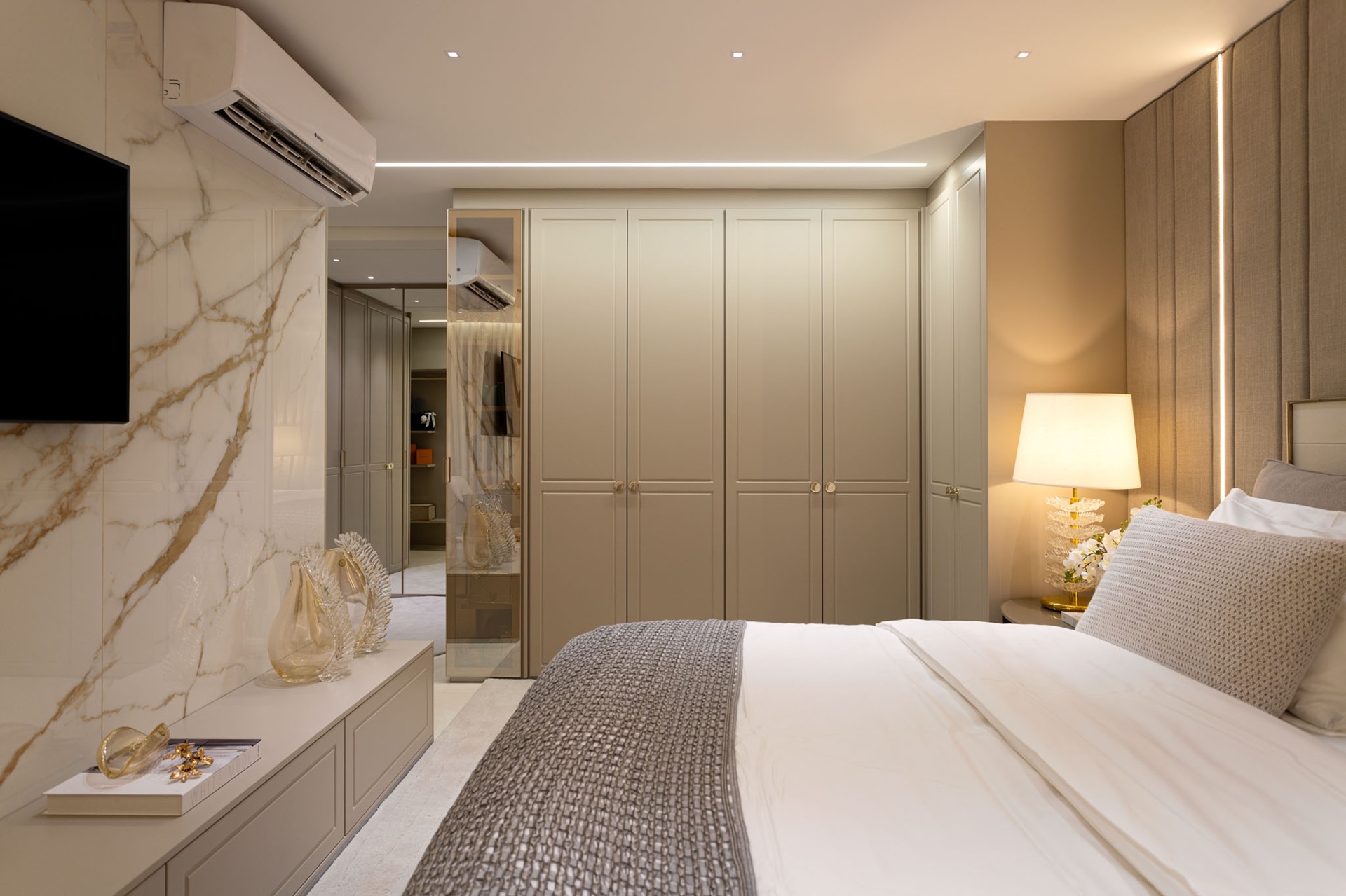 Quarto em tons claros como branco e bege, parede marmorizada branca e armários planejados