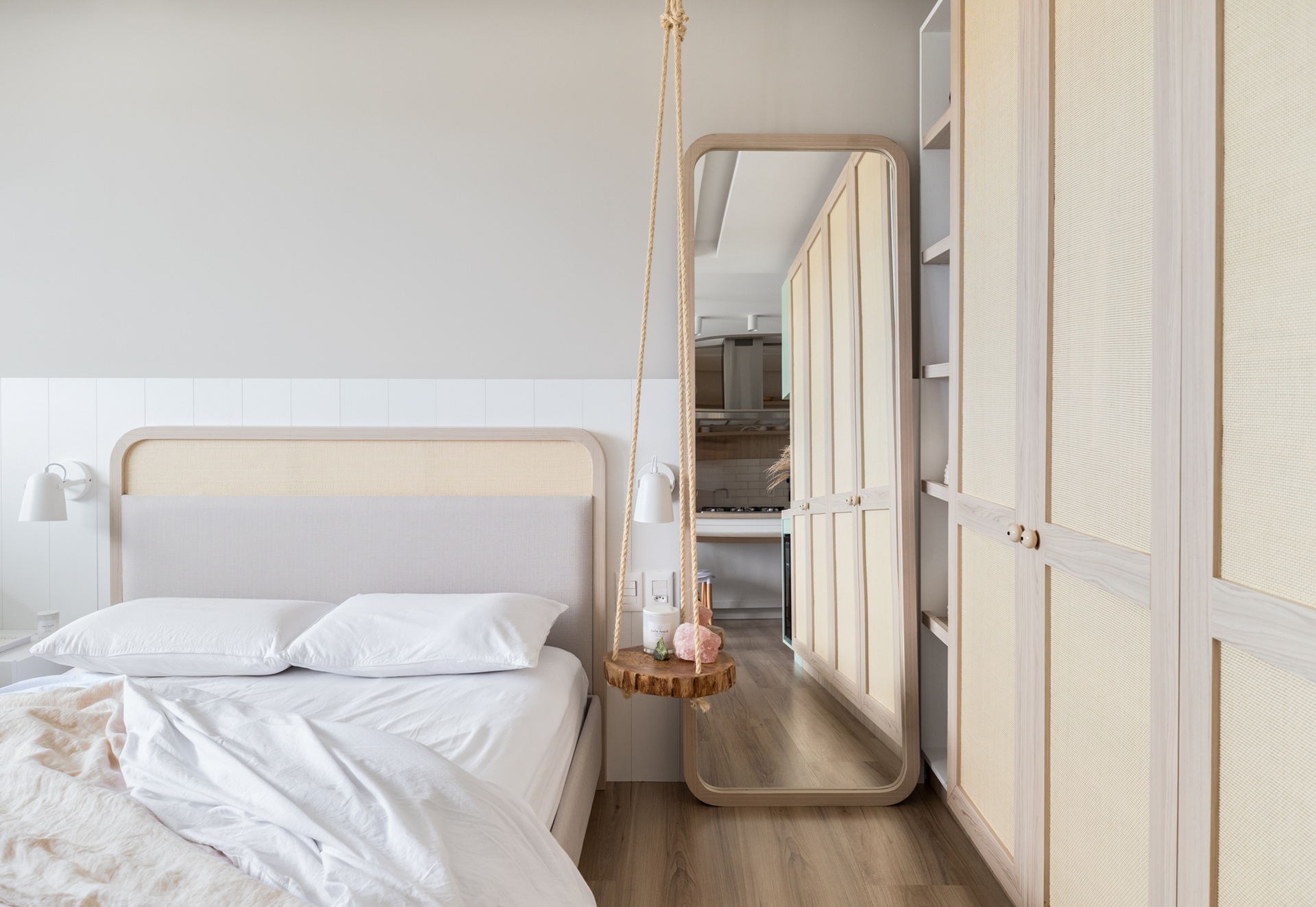 Quarto pequeno com piso amadeirado, cama de casal, espelho grande ao lado da cama e armário planejado
