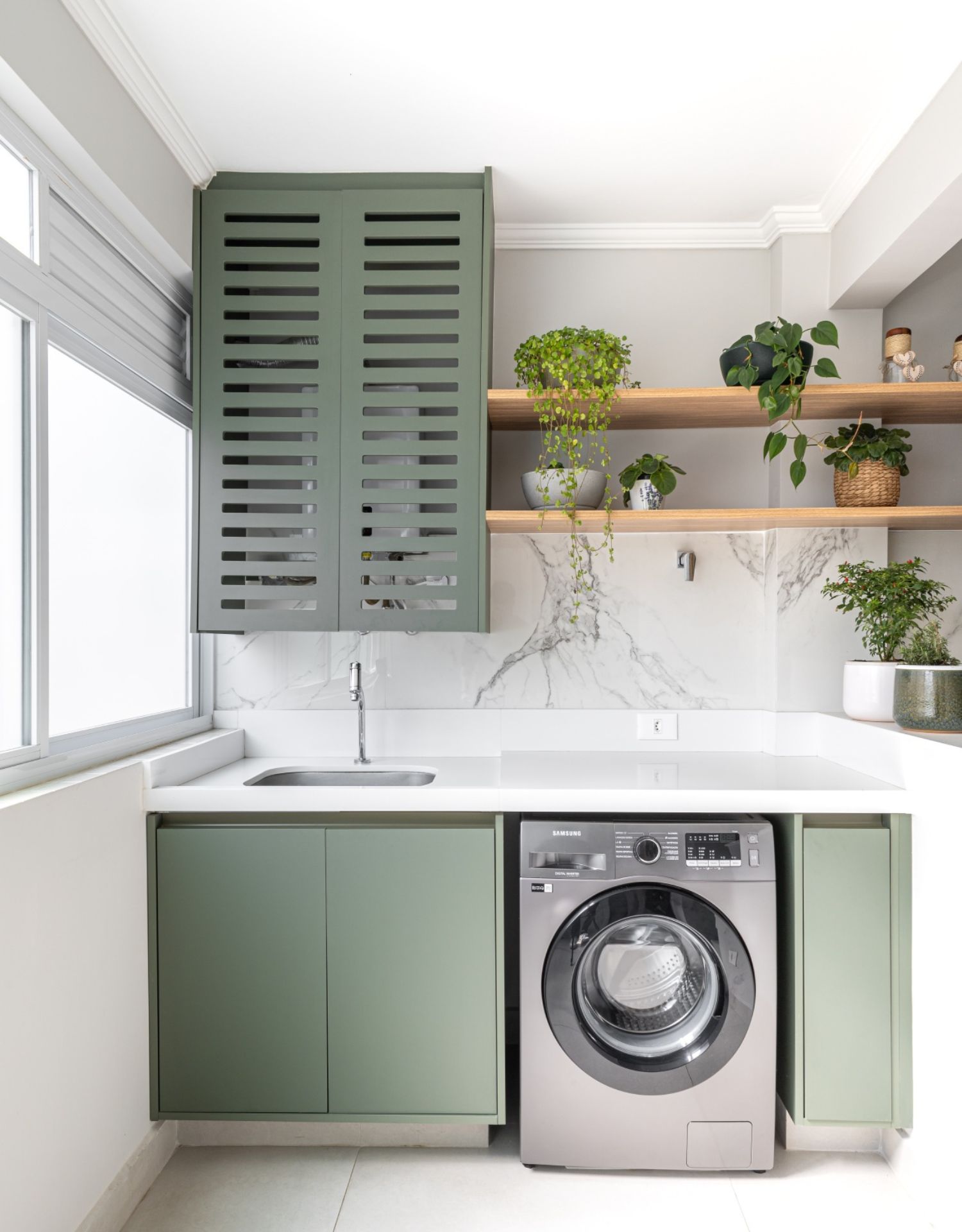 Lavanderia com mobiliário verde, bancada branca e eletrodoméstico em aço inox