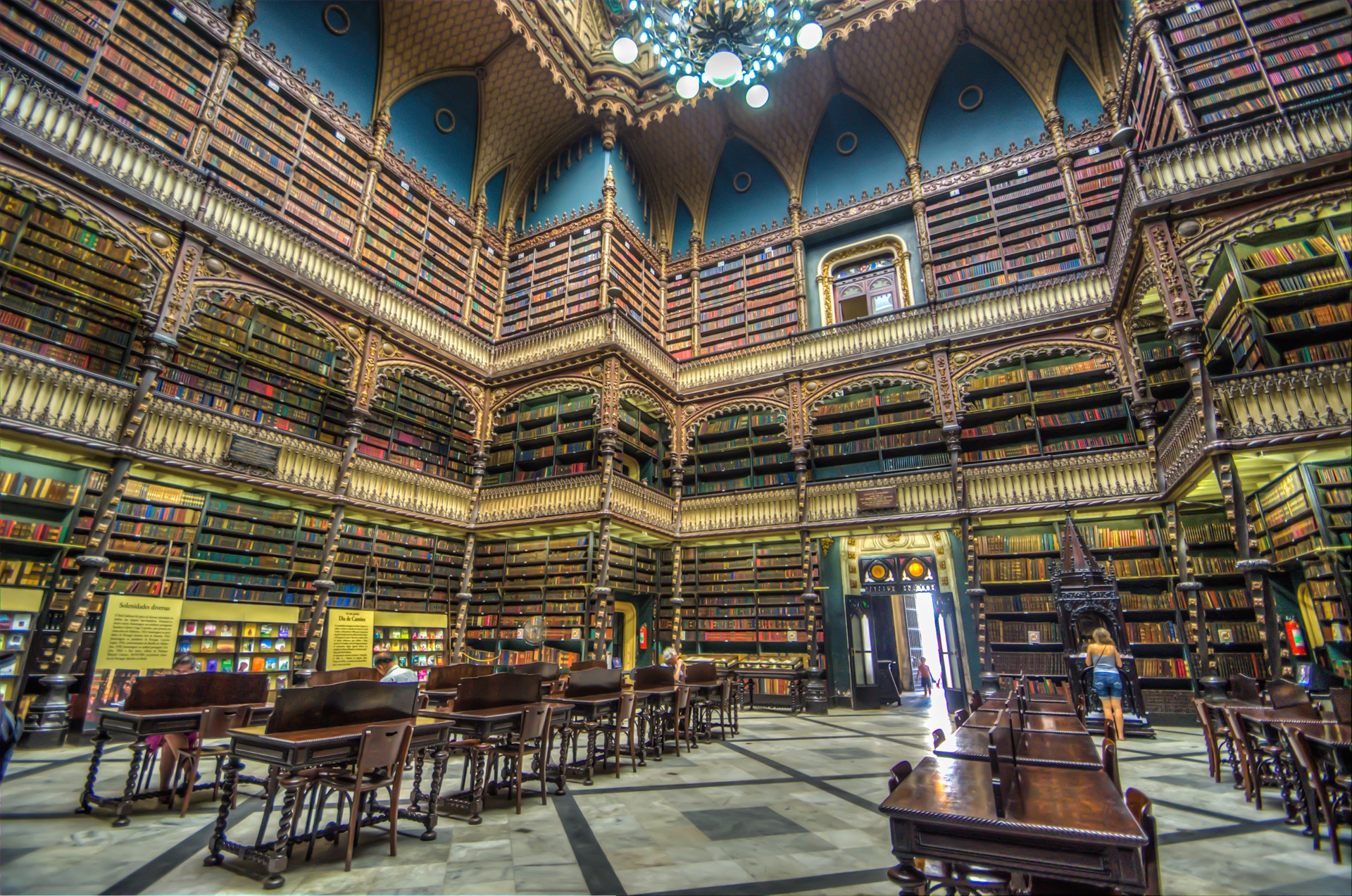 Interior do Real Gabinete Português de Leitura, no Rio de Janeiro, com estantes altas repletas de livros, estrutura em madeira entalhada, claraboia decorada e mesas de leitura dispostas sobre o piso de mármore