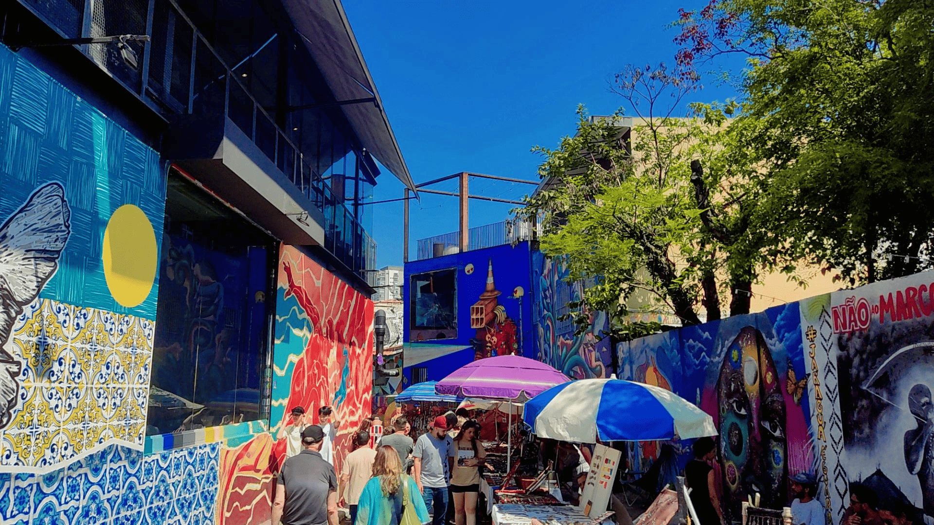 arte de rua Vista do Beco do Batman, na Vila Madalena, em São Paulo, com paredes cobertas por murais de street art multicoloridos, pessoas caminhando e bancas de artesanato sob guarda-sóis coloridos