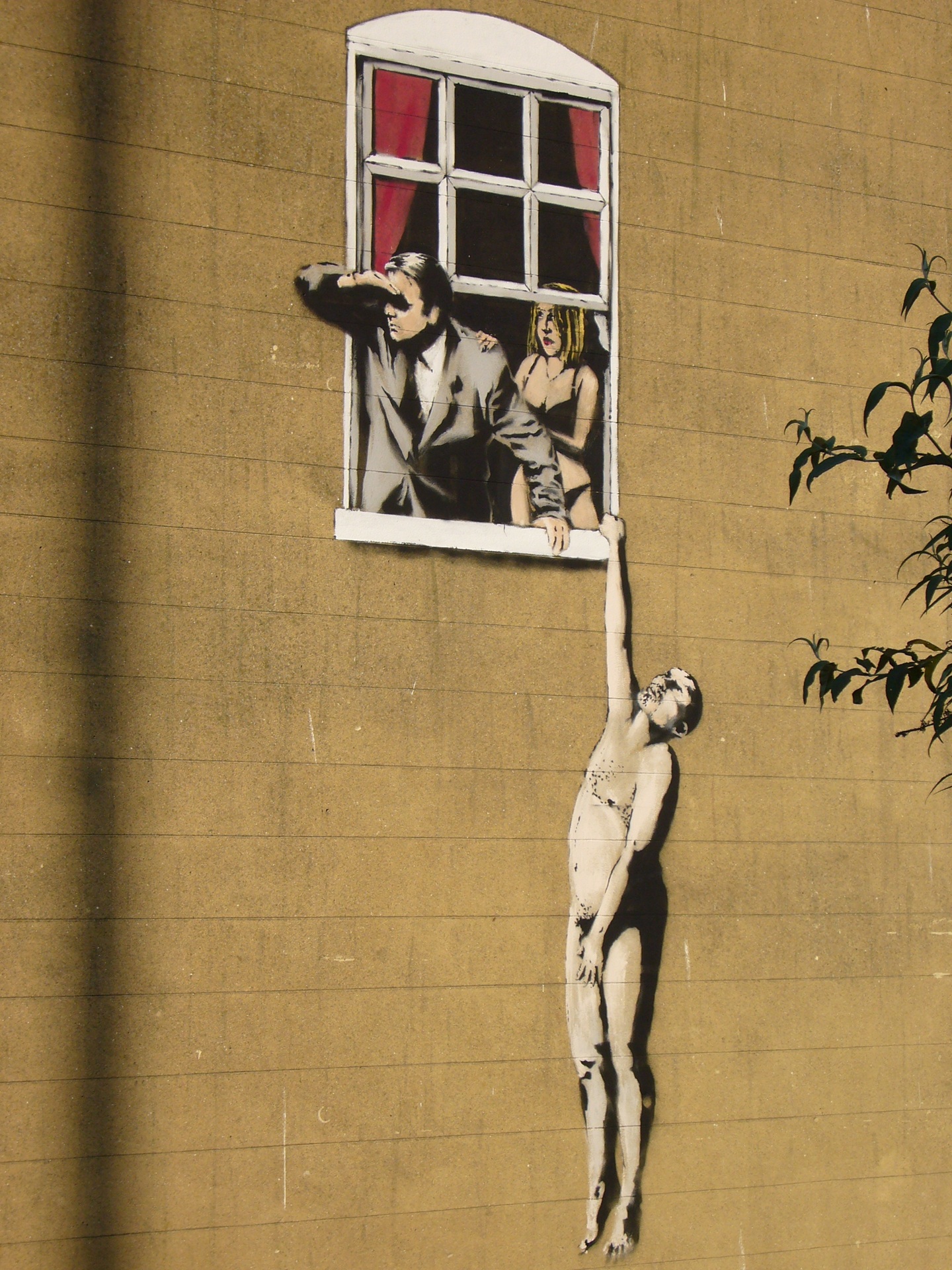 street art Mural Well Hung Lover, em Bristol, Inglaterra, criado pelo artista britânico Banksy. Feito com técnica de stencil, mostra um homem nu pendurado pela janela enquanto outro, de terno, observa a rua ao lado de uma mulher seminua