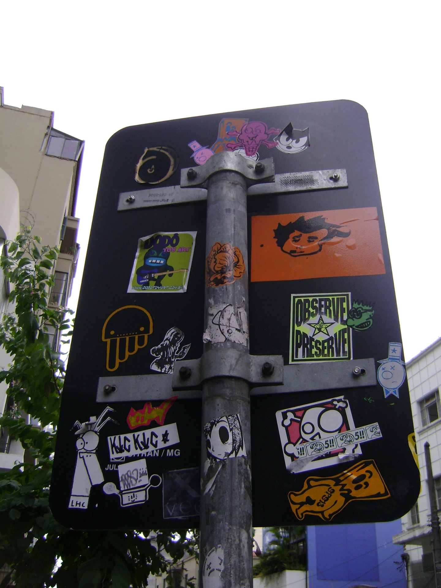 street art Placa de trânsito coberta por diversos adesivos coloridos de personagens, frases e símbolos, representando a técnica de sticker art