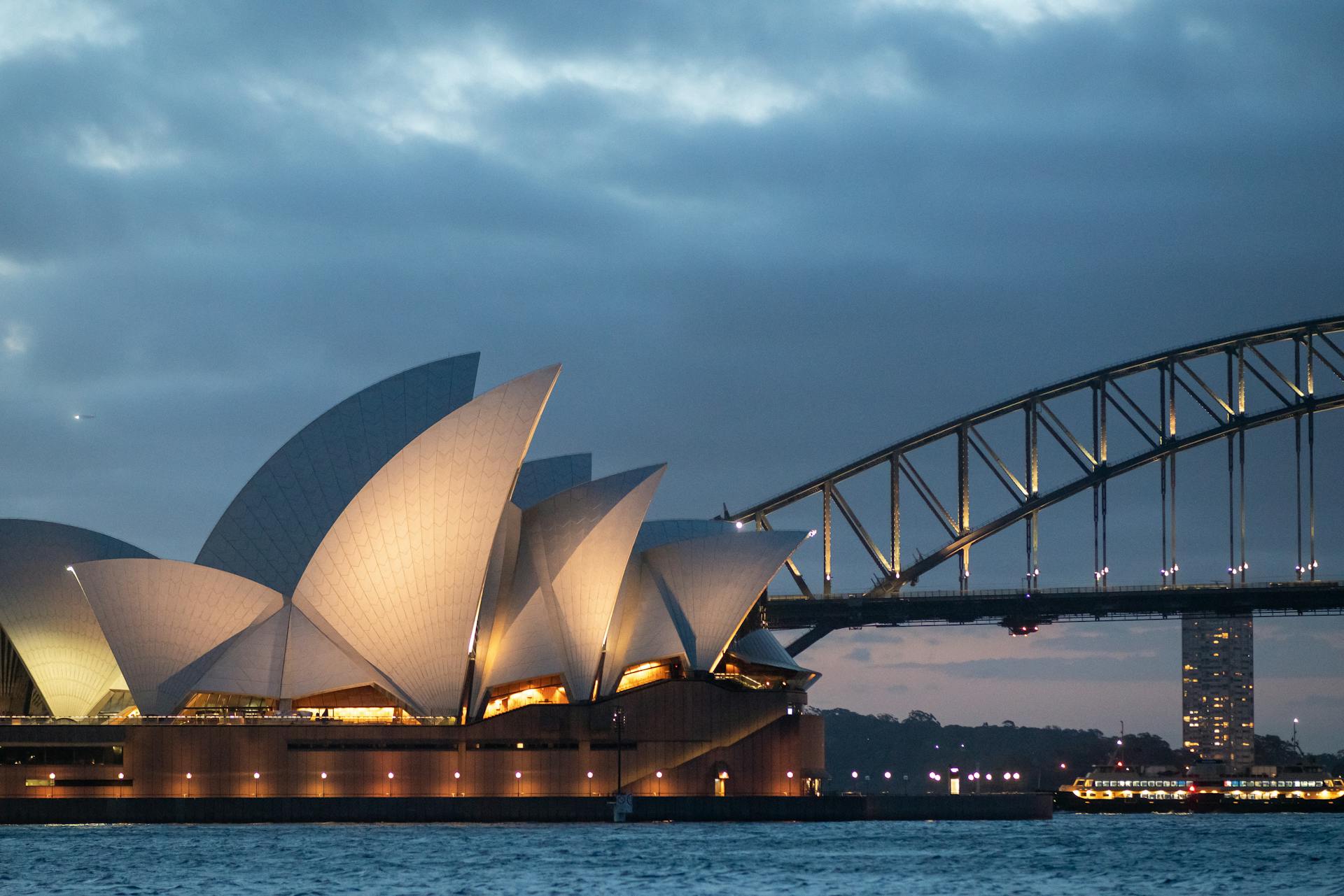 Vista noturna da Sydney Opera House com as suas icônicas velas iluminadas, em contraste com a Sydney Harbour Bridge ao fundo