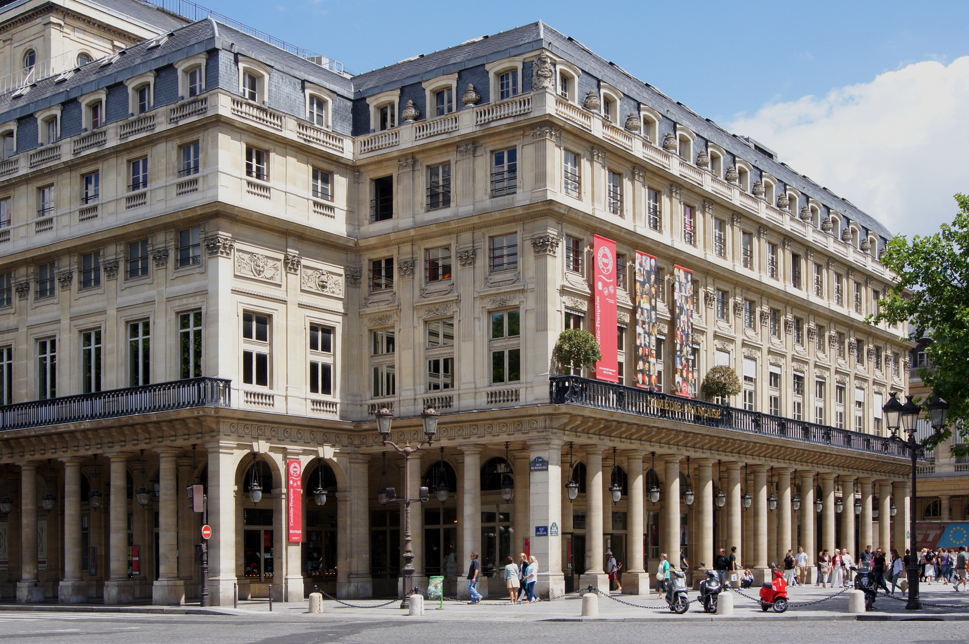 Fachada clássica do Comédie-Française, em Paris, com colunas, varandas e detalhes arquitetônicos ornamentais, localizada no Palais-Royal, com pessoas caminhando na calçada em frente ao edifício