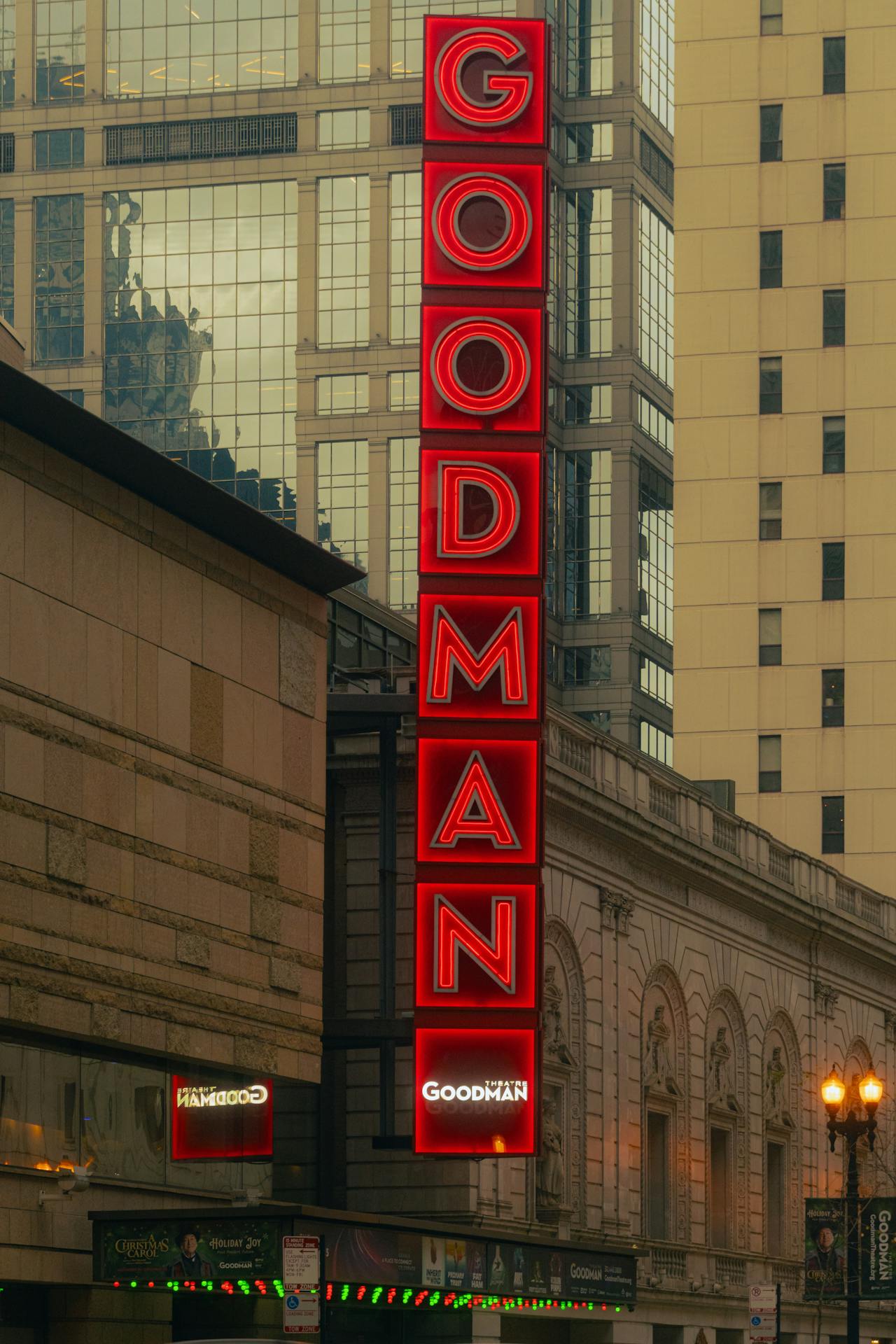 Letreiro vertical vermelho do Goodman Theatre, em Chicago, fixado na fachada do prédio, com arranha-céus refletindo na parte ao fundo