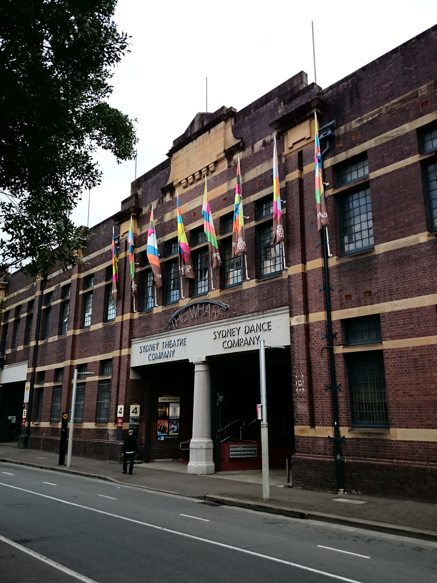 Fachada de tijolos do Sydney Theatre Company, em Sydney, Austrália, com bandeiras coloridas na entrada principal do edifício The Wharf