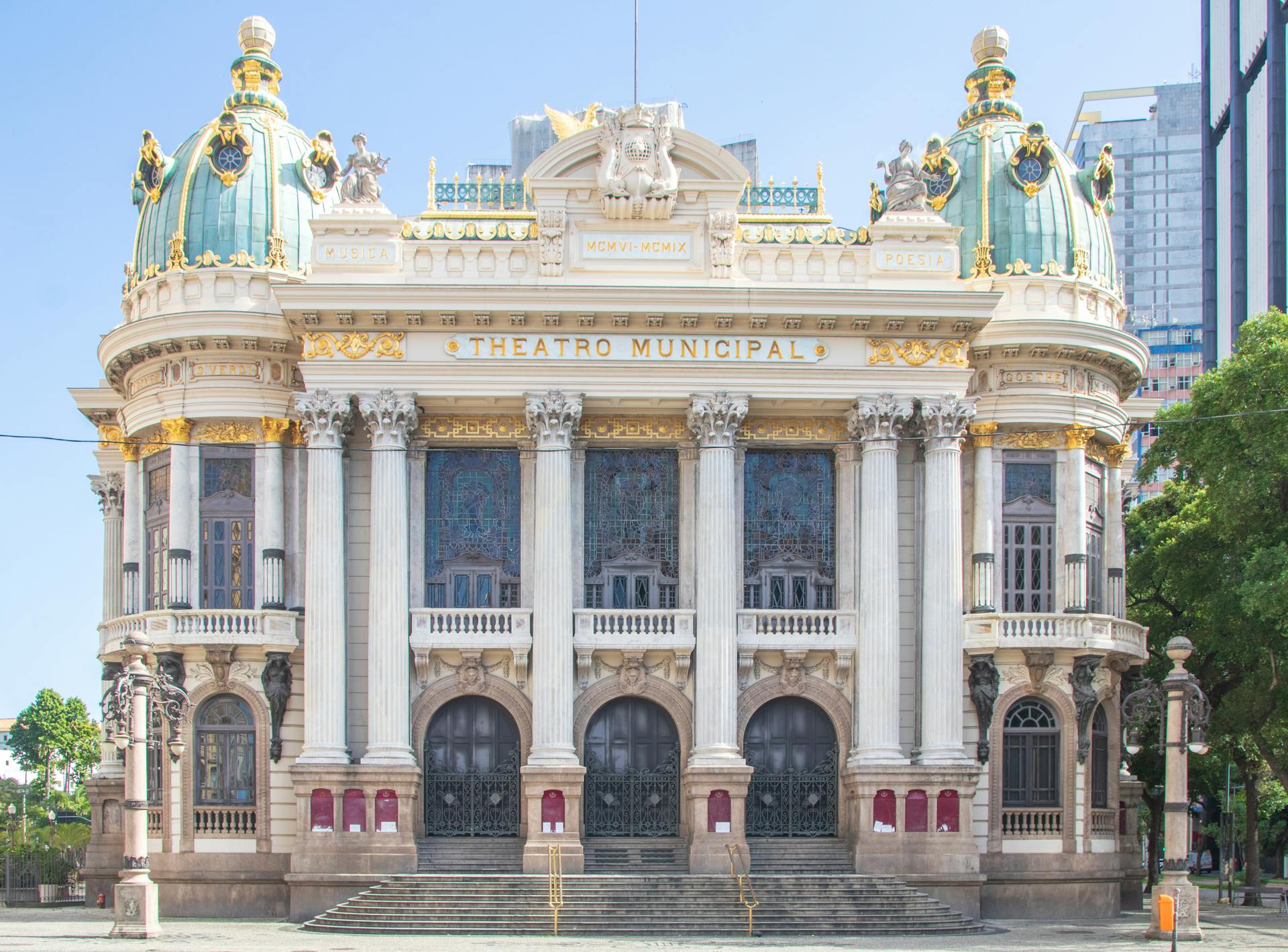 Fachada frontal do Theatro Municipal do Rio de Janeiro, com colunas, vitrais e cúpulas verdes ornamentadas em detalhes dourados, em estilo inspirado na Ópera de Paris