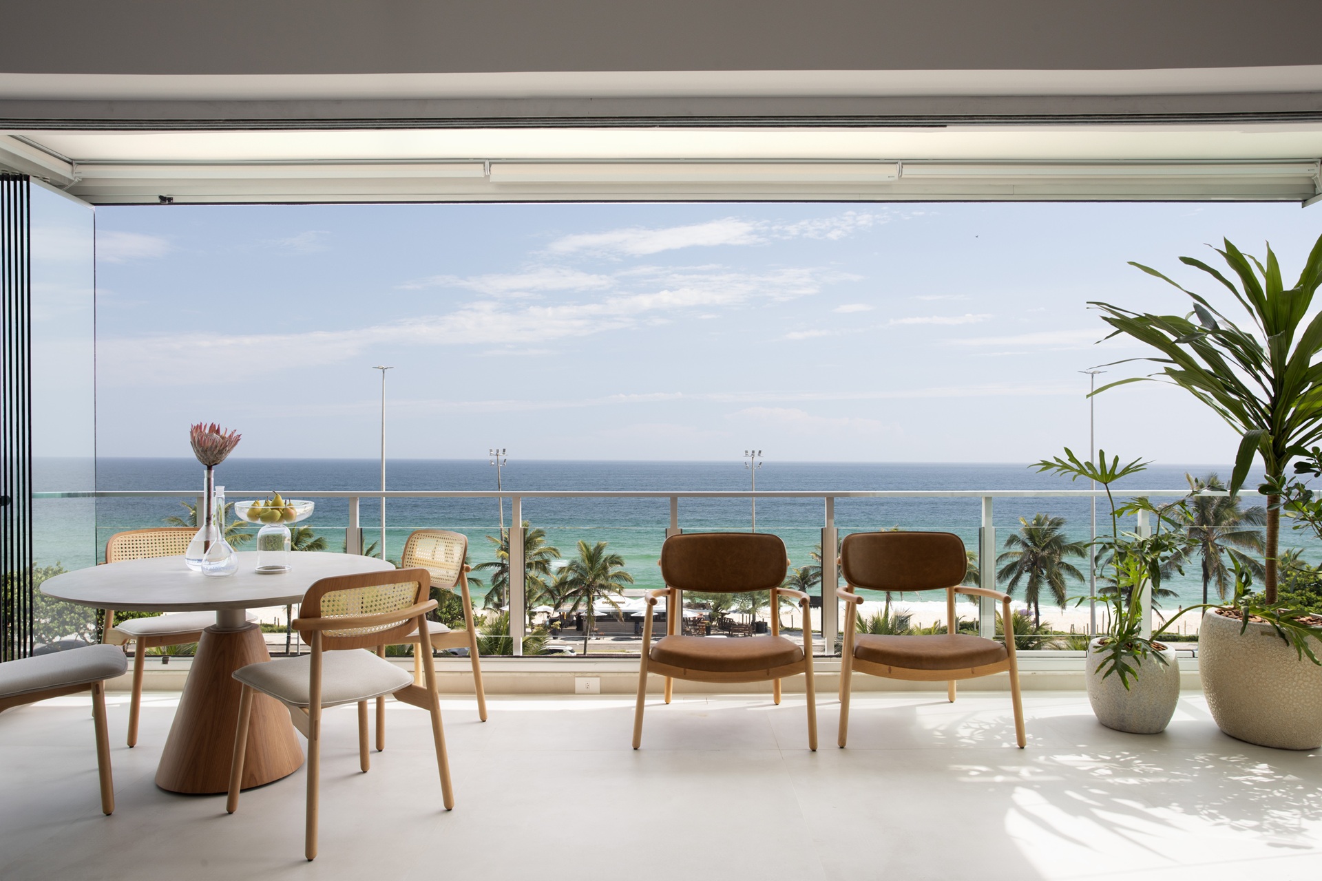 Varanda de apartamento com cadeiras e mesa de jantar redonda, com vista para o mar em dia de céu com poucas nuvens