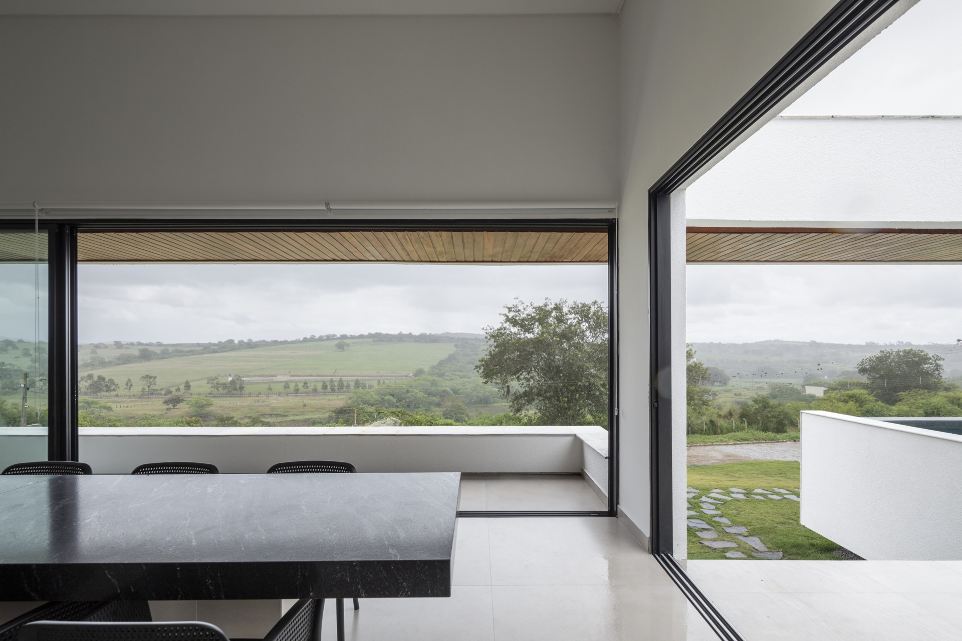 Sala de jantar com grandes aberturas de vidro e vista para área verde em agreste pernambucano