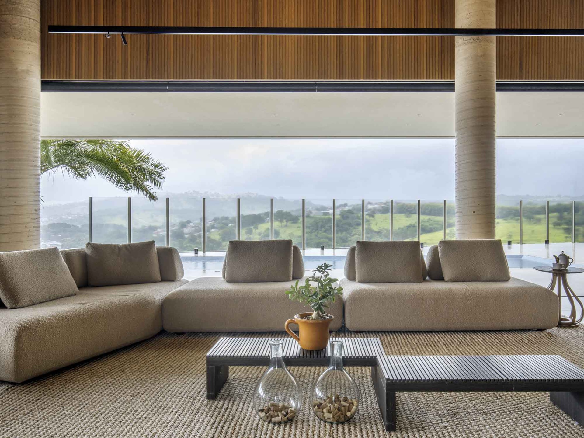 Varanda de apartamento com sofá em tom claro, mesa de cento e vista para área verde e ampla