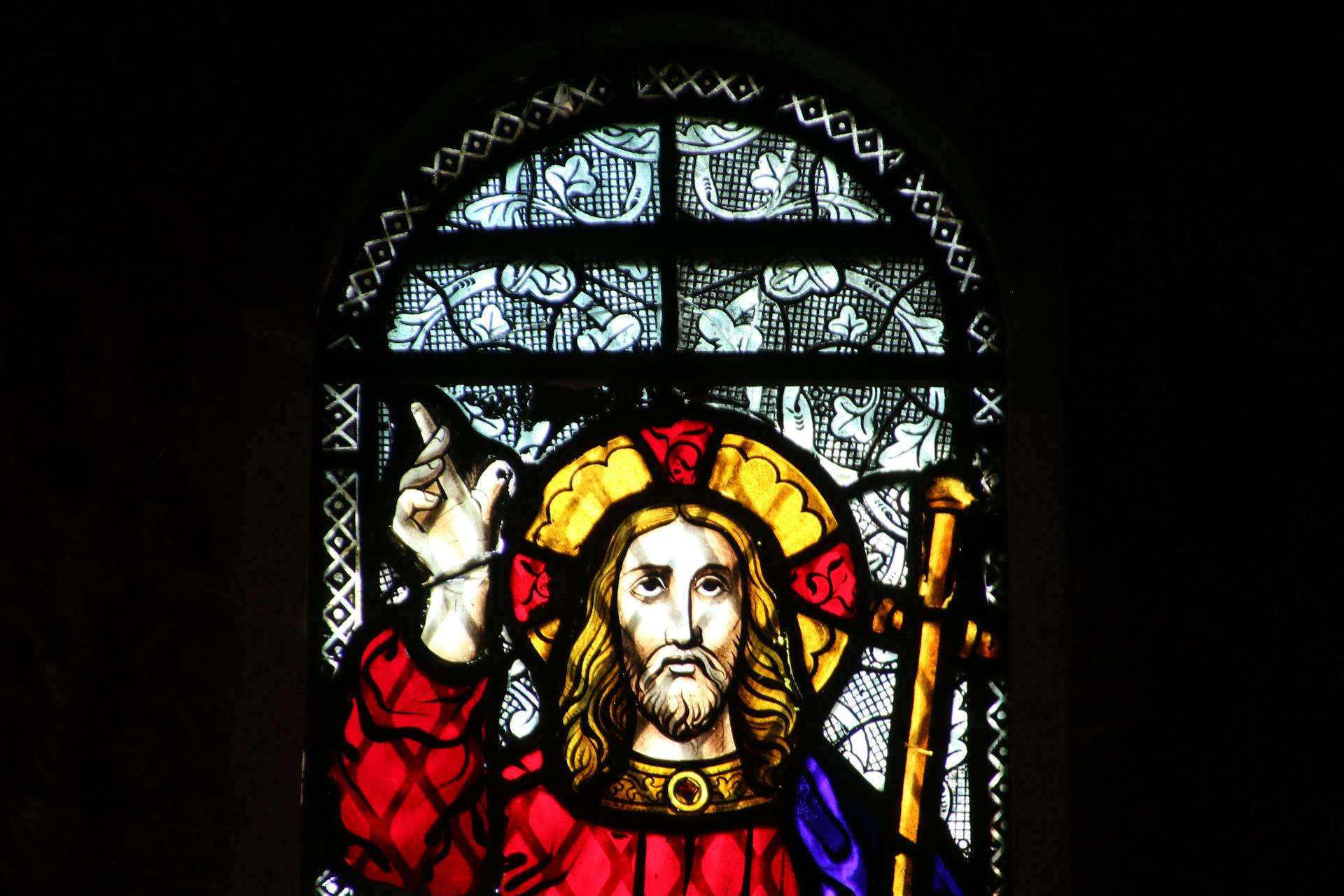 vitrais na arquitetura Vitral artístico em uma igreja de Knysna, África do Sul, retratando uma figura religiosa com túnica vermelha e auréola dourada, segurando um cajado. O fundo é composto por padrões florais e geométricos