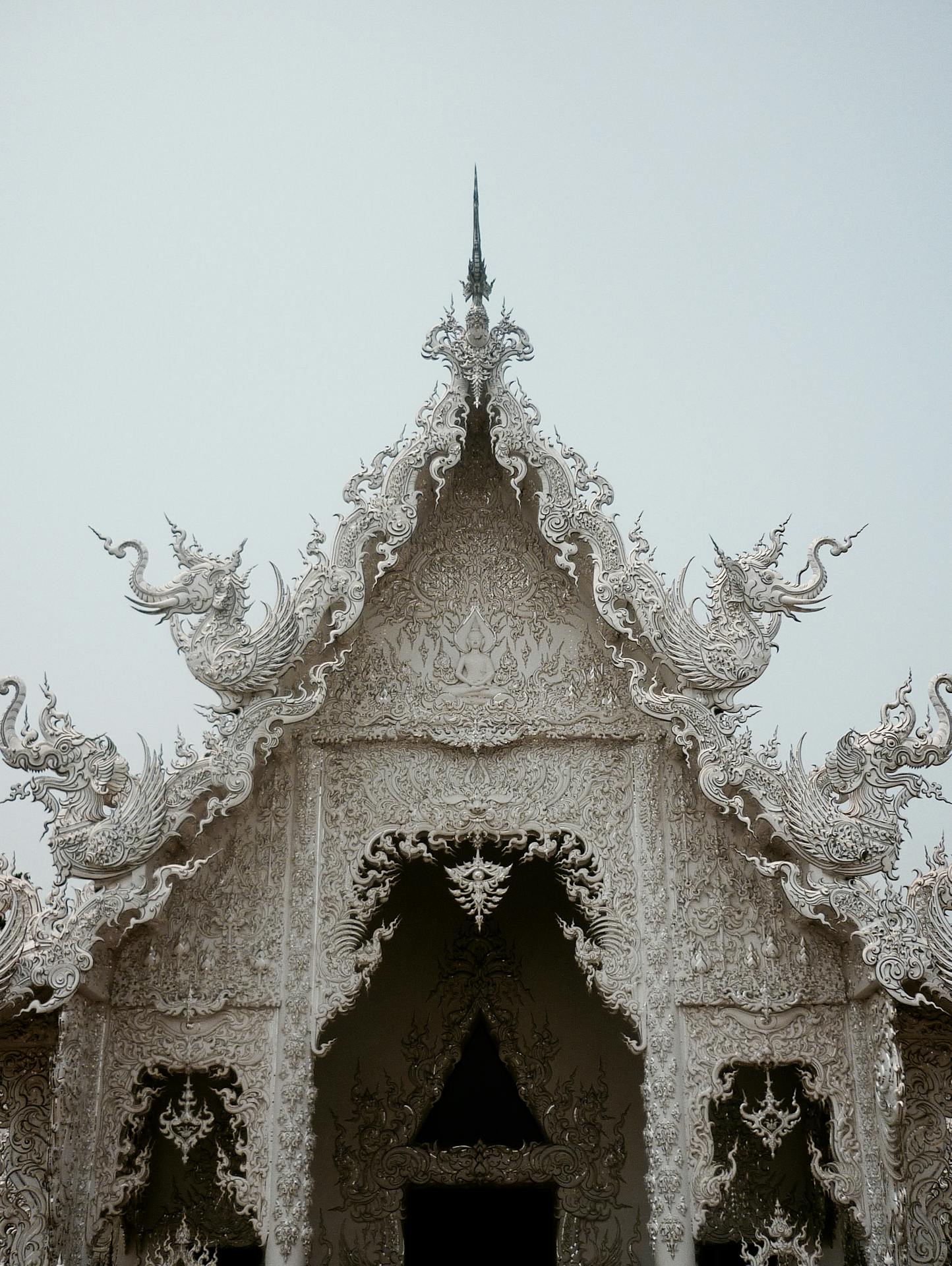 Close-up da fachada ornamentada do Wat Rong Khun, mostrando entalhes intricados, figuras mitológicas e padrões simétricos em relevo branco
