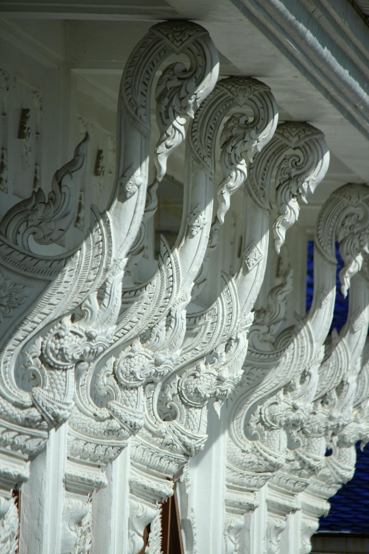 Close-up das esculturas brancas ornamentadas do Wat Rong Khun, o Templo Branco de Chiang Rai, mostrando arabescos e figuras mitológicas em alto-relevo