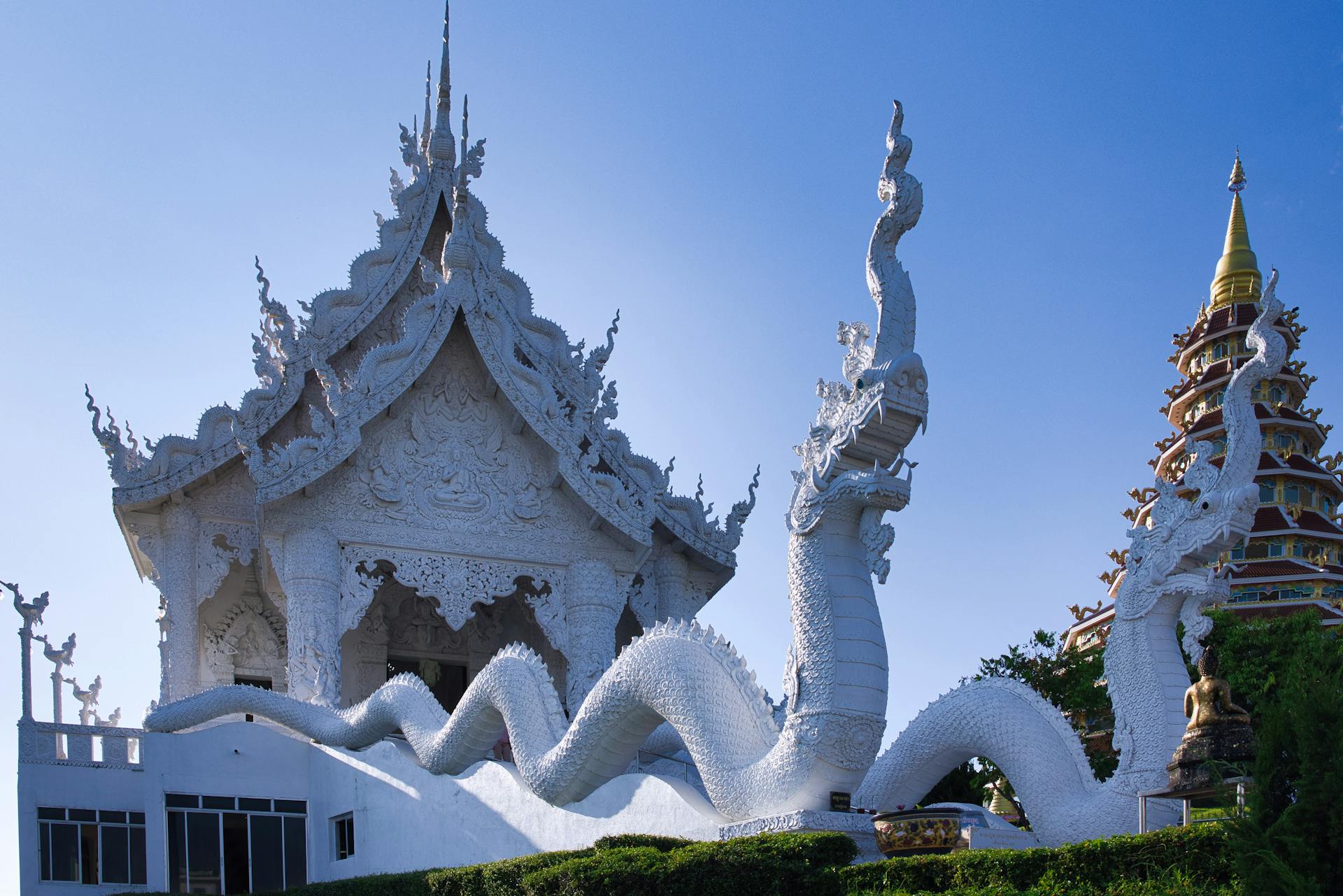 Vista ampla do Wat Rong Khun, o Templo Branco de Chiang Rai, com esculturas de dragões brancos sinuosos diante da fachada ornamentada