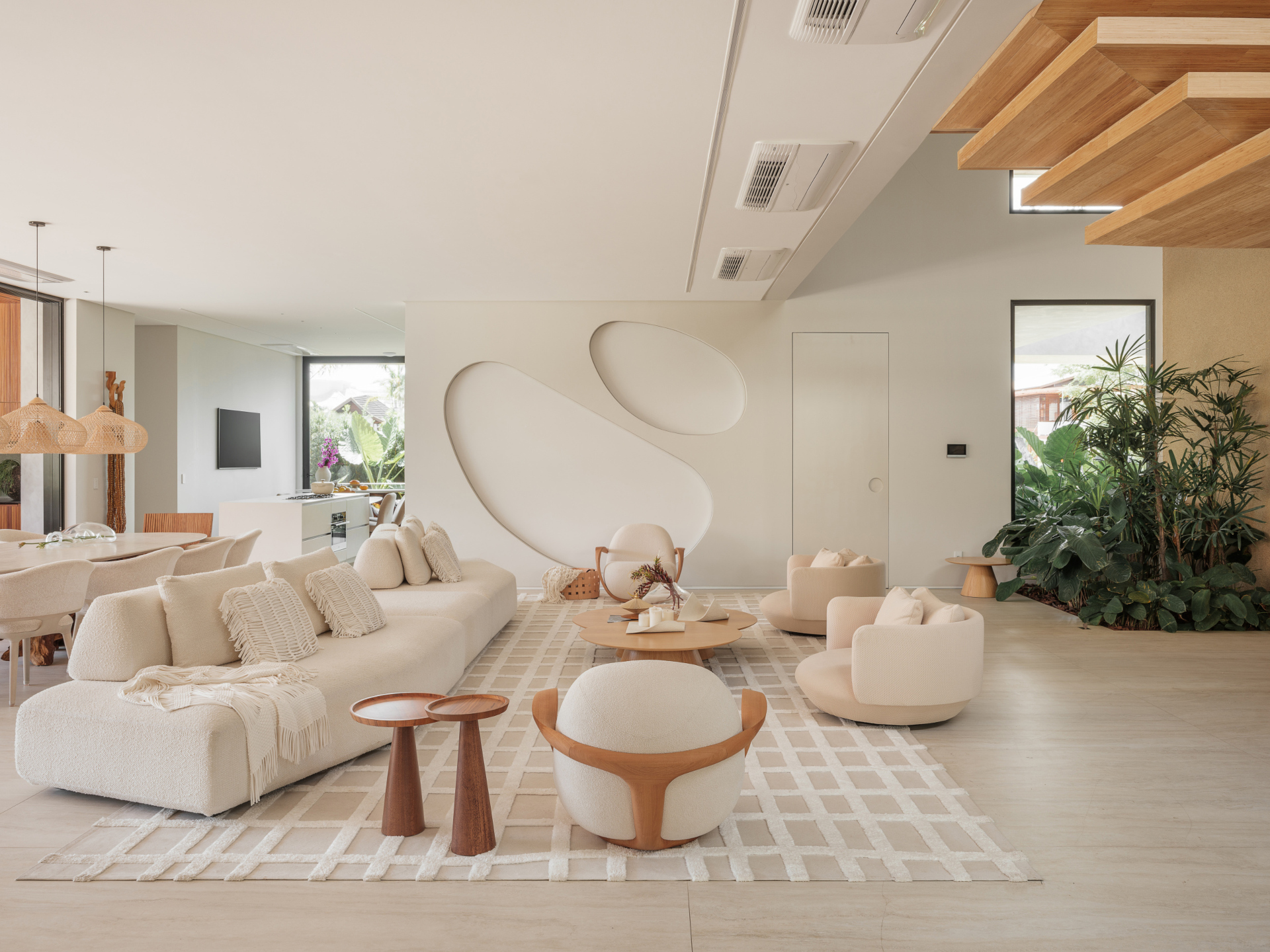 Sala ampla em tons neutros e claros com sofá e poltronas em formato orgânico.