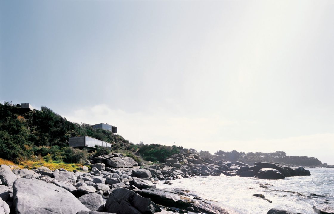 Área de praia com pedras perto da areia e casa contemporânea ao fundo