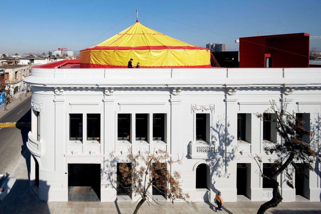 Fachada de prédio histórico pintado de branco com lona amarela e vermelha no terraço