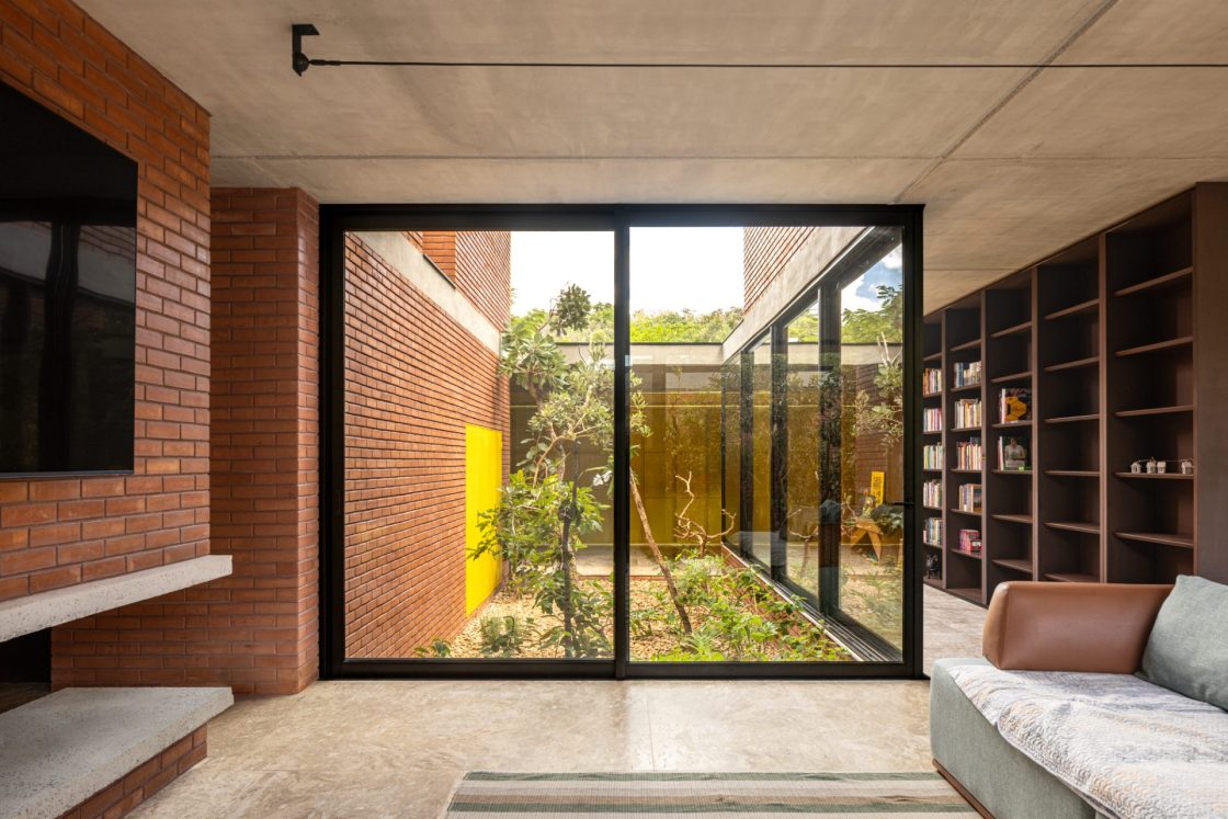 Living com paredes de vidro que dão vista para jardim interno e estantes ao fundo