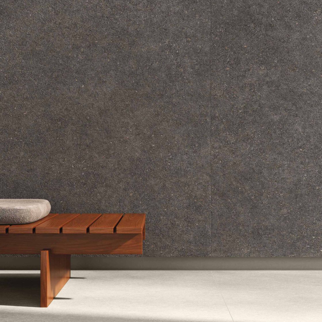 Detalhe de parede com Coal Frieze, porcelanato da linha Kalks, com banco de madeira em frente
