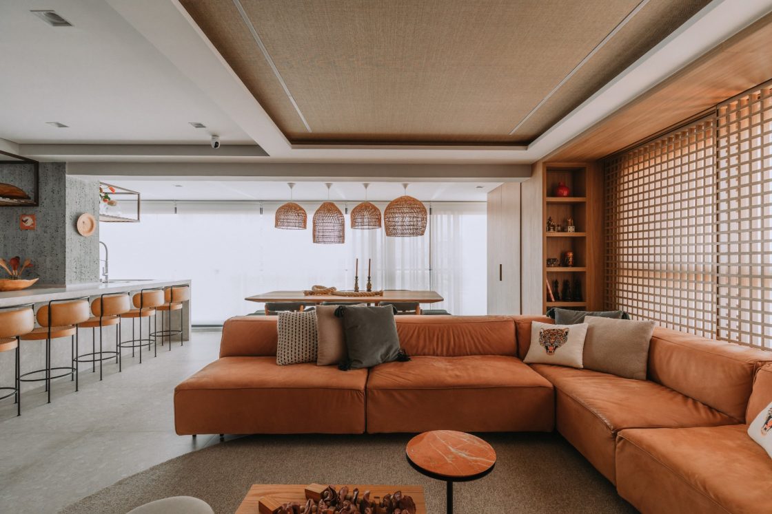 Sala ampla integrada à cozinha e à sala de jantar, com sofá em "L" em tom terracota