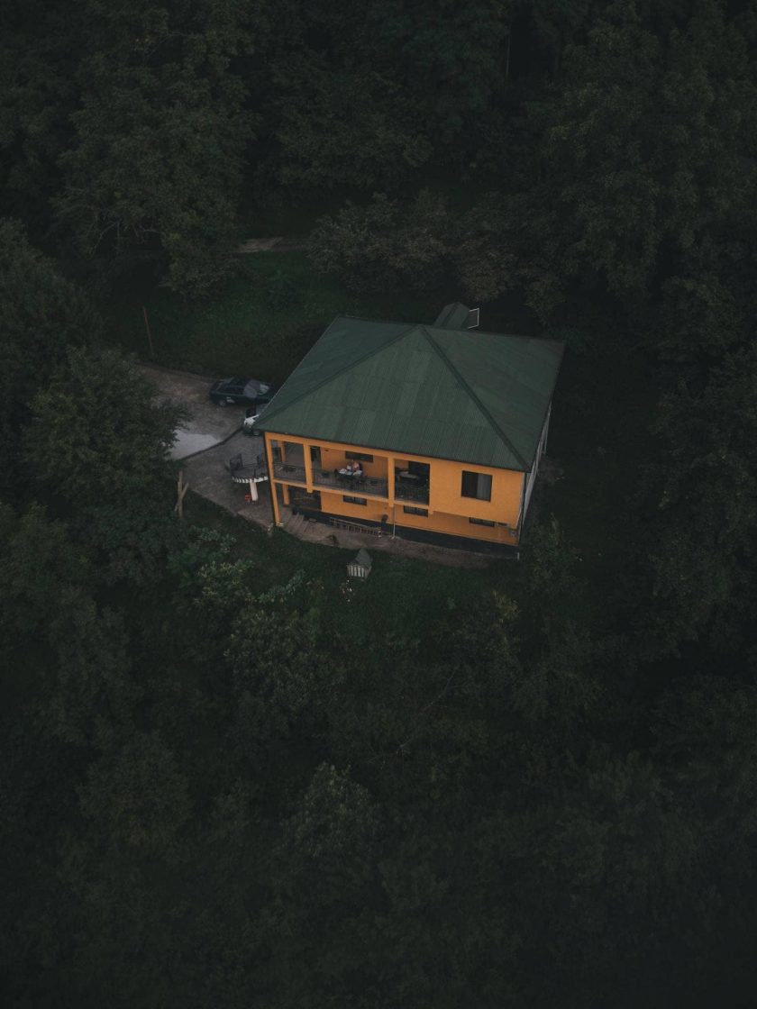 Casa cercada por floresta densa vista de cima, com acesso restrito por estrada estreita em área de vegetação fechada