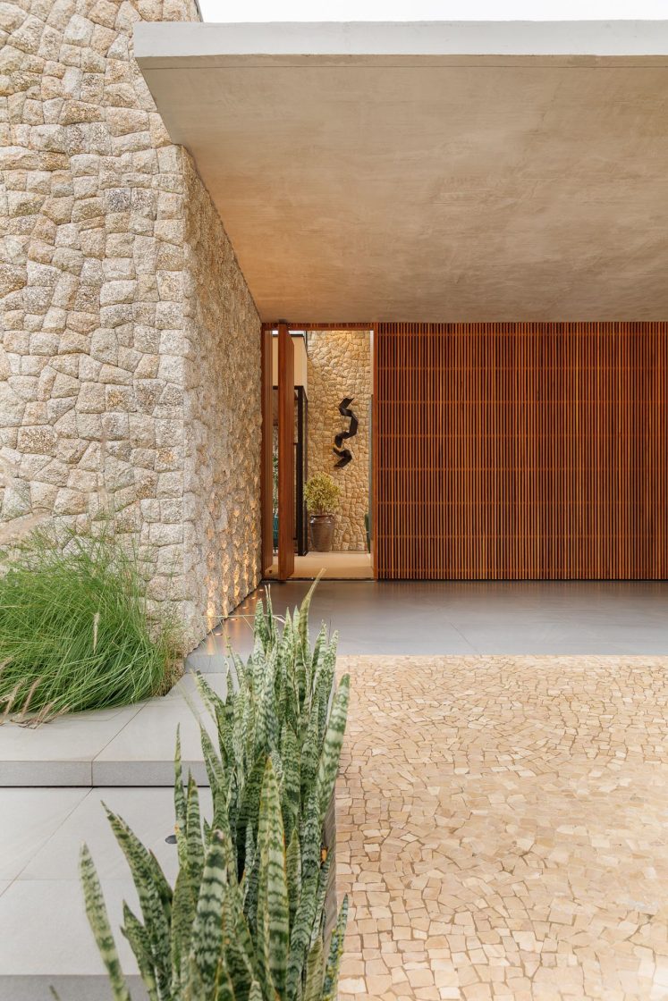 Fachada de casa com parede em pedra natural e subida de garagem com piso de pedra portuguesa