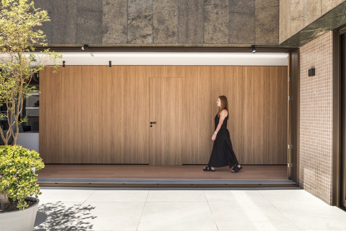 Mulher andando em frente a parede amadeirada com porta, na varanda do Apartamento RG