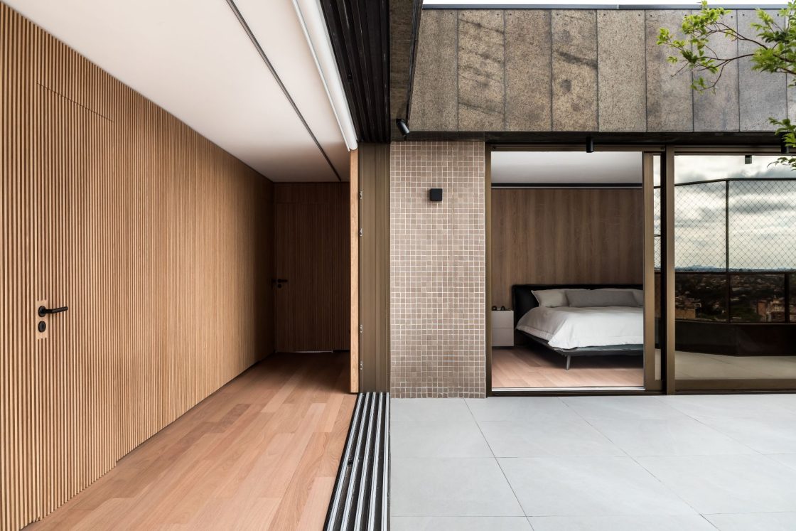 Quarto de casal com porta de vidro ampla e aberta, visto a partir da varanda do apartamento