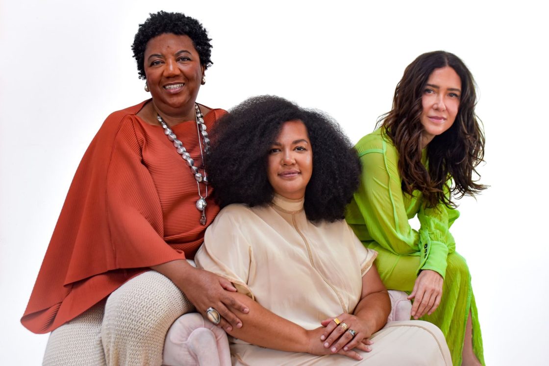 Retrato coletivo de Rosana Paulino, Diane Lima e Adriana Varejão, integrantes do projeto “Comigo Ninguém Pode” para o Pavilhão do Brasil na Bienal de Veneza 2026, posando em estúdio com roupas contemporâneas e fundo neutro claro