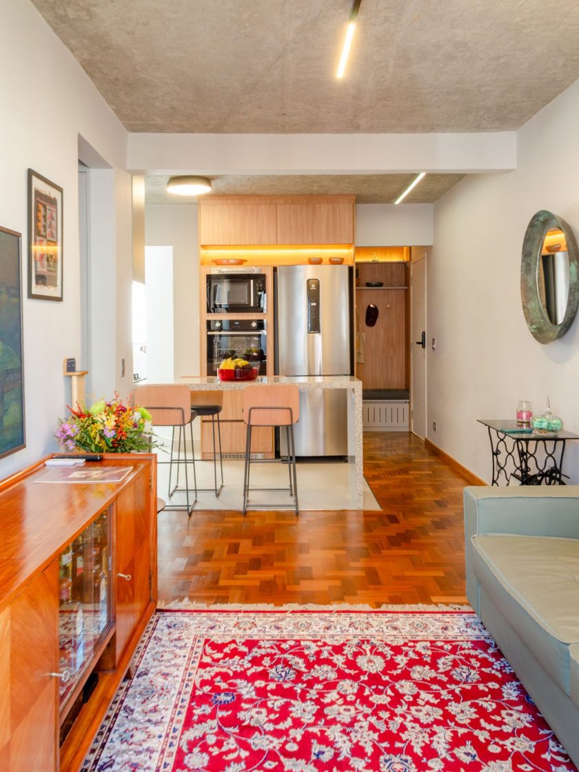 piso em porcelanato ajuda a delimitar os espaços entre cozinha e sala com piso de taco, enquanto o tapete persa, o vaso com flores e a antiga máquina de costura