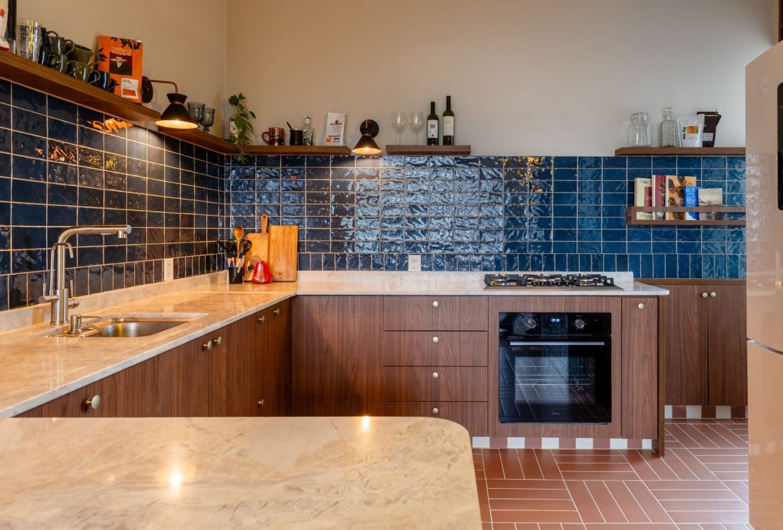 Cozinha com backsplash de revestimento cerâmico azul, armários em madeira escura, bancada em mármore e piso em cerâmica em paginação trama de cesta basket weave