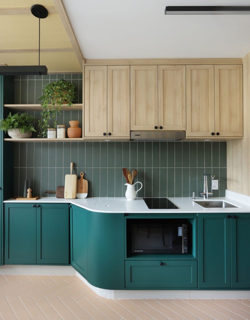 Cozinha com armários inferiores em verde-esmeralda, armários superiores em madeira clara e backsplash de revestimento cerâmico verde em paginação vertical