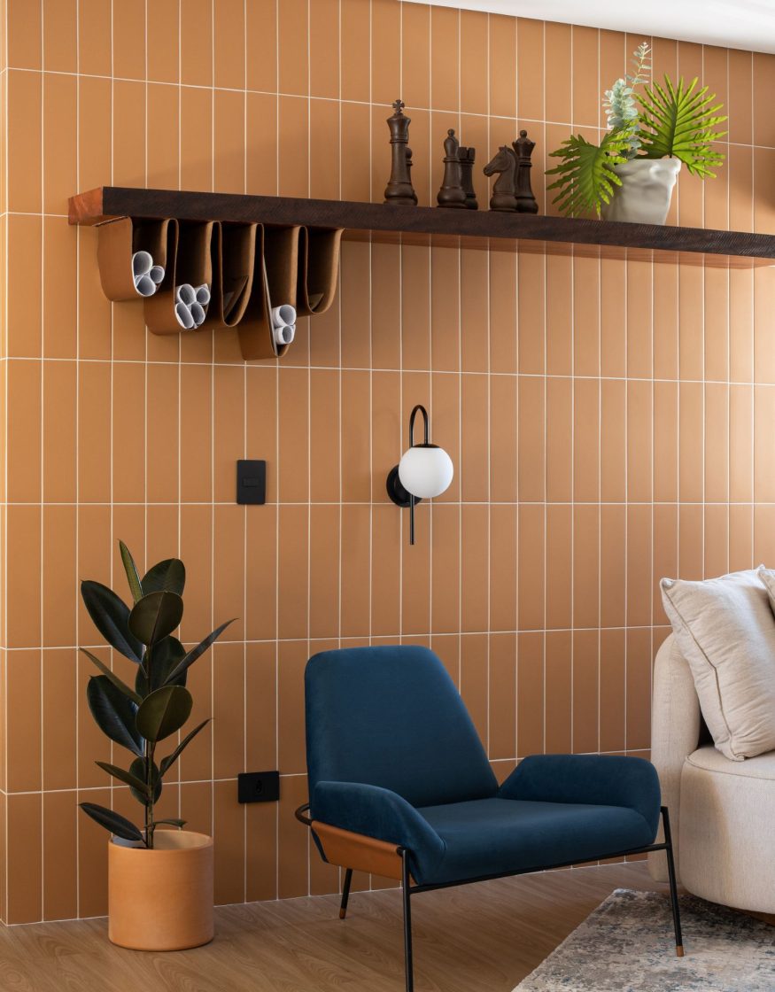 Sala de estar com parede revestida em cerâmica terracota em paginação vertical, poltrona estofada em azul-petróleo e prateleira em madeira escura