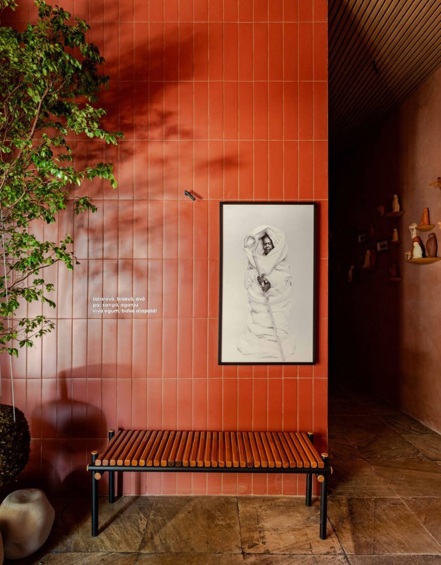 Parede revestida com revestimentos cerâmicos retangulares na cor terracota, dispostas em paginação vertical. No centro da parede, há uma obra de arte em preto e branco emoldurada
