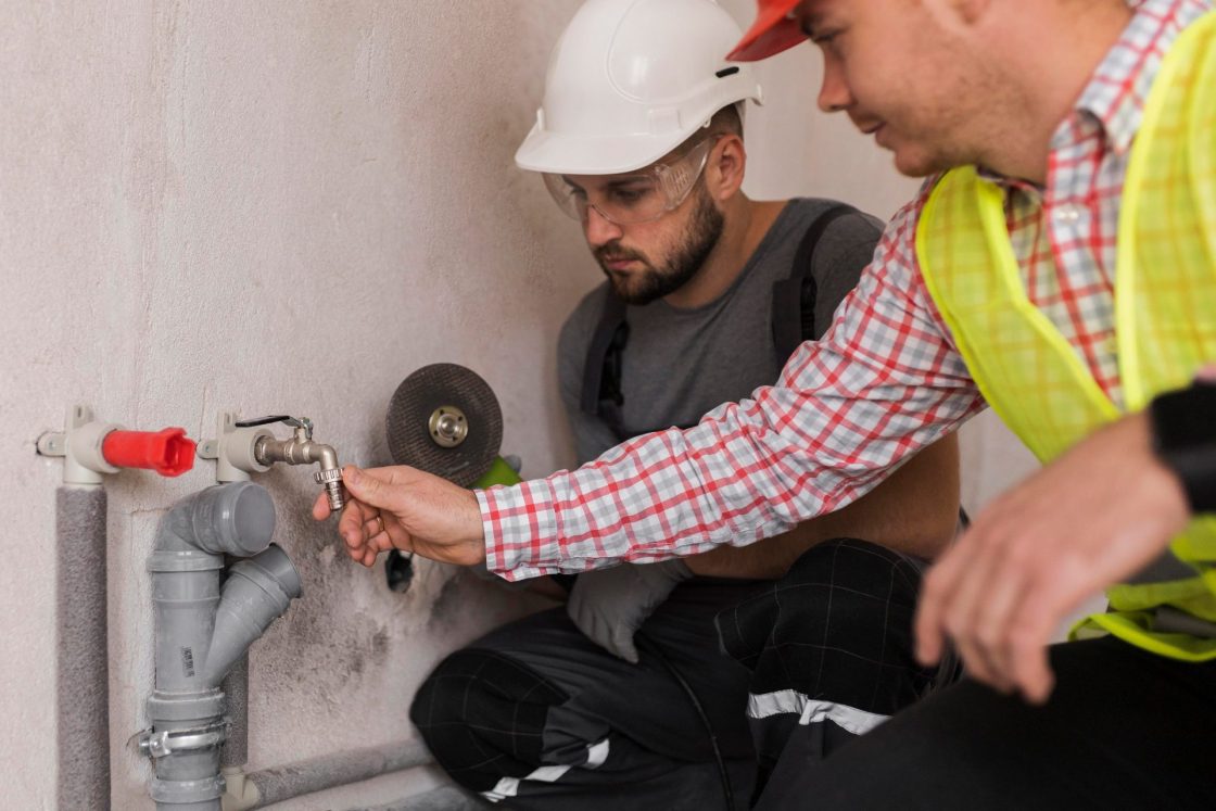 Dois homens com capacete, trabalhando em obra e inspecionando torneira