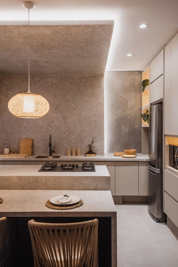 Cozinha em tons neutros e terrosos, com ilha com cooktop e luminária pendente por cima