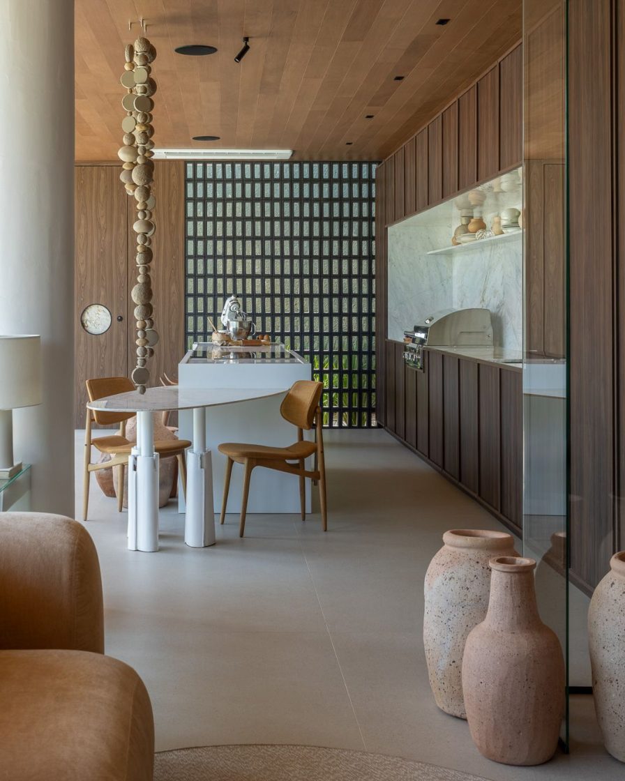 Cozinha com ilha em tons neutros e mobiliário em madeira escura, com parede em cobogó ao fundo
